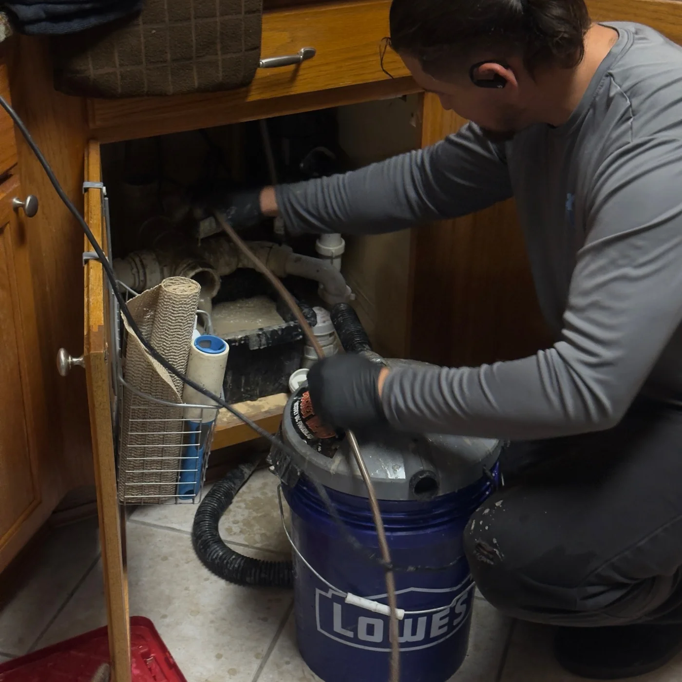 Technician working on plumbing inside a kitchen sink cabinet